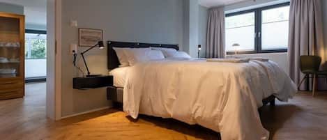 Ein Schlafzimmer mit einem großen Bett, einem Nachttisch, einer Lampe und einem Fenster mit Vorhängen.