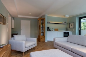 A modern living room with a sofa and armchair, a wooden cabinet, and a kitchen area with cabinets and a countertop. - Holiday apartment in Wildeshausen with Wi-Fi (Wildeshausen)