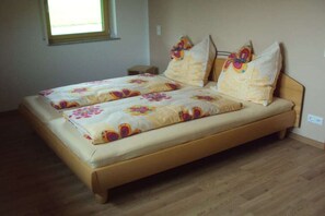 Una cama doble con ropa de cama floral en una habitación con suelo de madera y ventana.