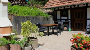 An outdoor patio with a table and chairs, surrounded by potted plants and a building with a tiled roof. - ||------------------storage building------------|| (Hornberg)