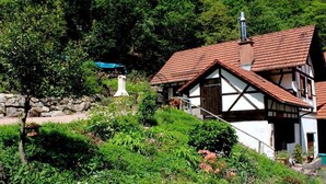 A traditional half-timbered house with a sloped roof, surrounded by lush greenery and a stone wall. - ||------------------storage building------------|| (Hornberg)