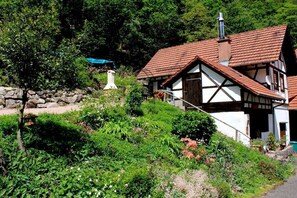 A traditional half-timbered house with a sloped roof, surrounded by lush greenery and a stone wall. - ||------------------storage building------------|| (Hornberg)