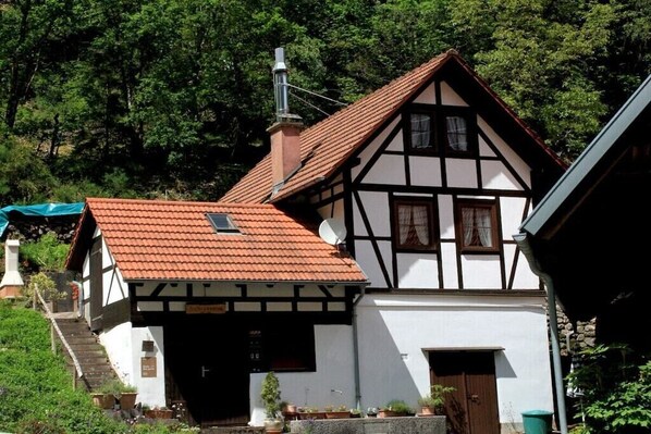 A traditional half-timbered house with a red-tiled roof, a chimney, and a small satellite dish. - ||------------------storage building------------|| (Hornberg)
