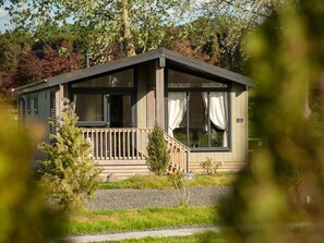Een gelijkvloers vakantiehuisje met een houten terras, grote ramen en een klein voortuintje.