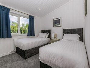 Een slaapkamer met twee bedden, een raam met gordijnen, een nachtkastje met een lamp en een lijst met een afbeelding aan de muur.