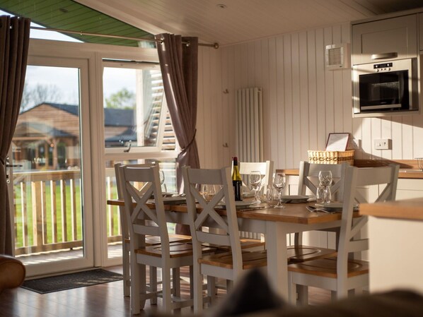 Een eethoek met een tafel voor vier personen, witte stoelen en uitzicht op de omgeving door een glazen deur.