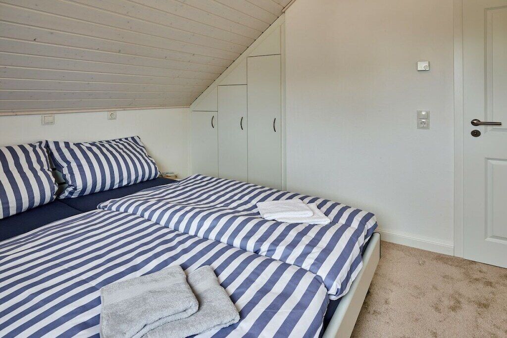 A bedroom with a bed, striped bedding, a white door, and a ceiling with wooden beams.