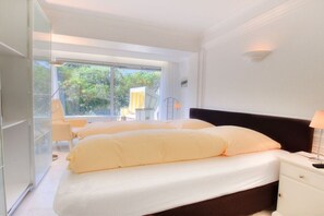 Ein Schlafzimmer mit einem Bett, einem Nachttisch und einem Fenster mit Blick auf Grün.