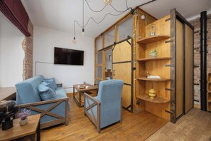 A modern living room with a blue sofa, wooden shelves, and a TV mounted on the wall. - Loft Apartment in Warsaw | Close to Metro | Pet Friendly (Warszawa)