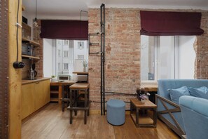 A compact living space with a brick wall, wooden furniture, a blue sofa, and a kitchen area with a coffee machine. - Loft Apartment in Warsaw | Close to Metro | Pet Friendly (Warszawa)
