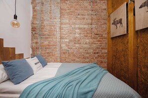 A bed with a blue blanket, a light bulb, a brick wall, and a framed picture of a moose. - Loft Apartment in Warsaw | Close to Metro | Pet Friendly (Warszawa)