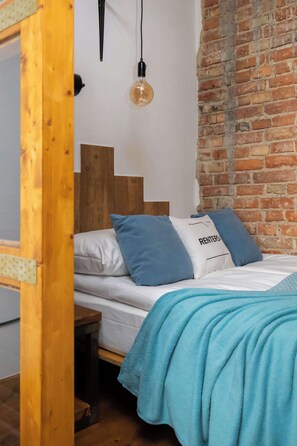 A bedroom with a wooden headboard, a single bed with blue and white bedding, a blue blanket, and a brick wall. - Loft Apartment in Warsaw | Close to Metro | Pet Friendly (Warszawa)
