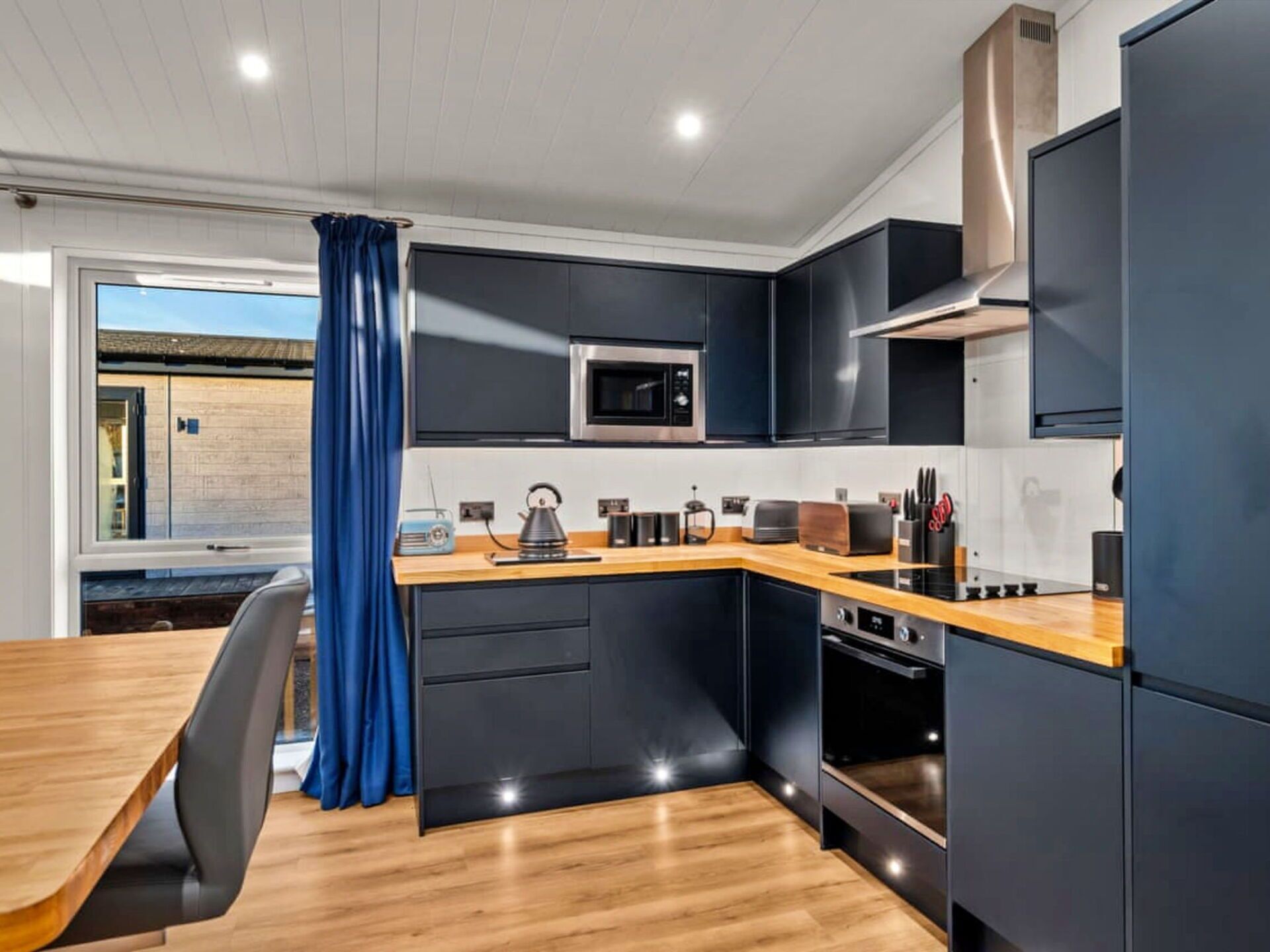 A modern kitchen with black cabinets, a wooden countertop, and stainless steel appliances.