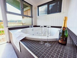 A hot tub with two glasses and a bottle of champagne on a tiled surface.