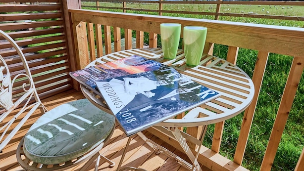 Een houten terras met een tafel, stoelen, een tijdschrift en twee groene glazen.