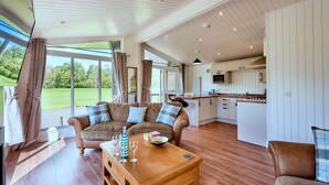 Een ruime woonkamer met een houten salontafel, een bank en uitzicht op een groen landschap door grote ramen.