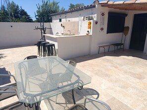 An outdoor patio with a glass table and chairs, a barbecue grill, and a small seating area. - Quiet country home (Pernes-les-Fontaines)