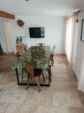 Un espace repas avec une longue table recouverte d’une nappe à motifs tropicaux, entourée de chaises dont les montants sont en bois et ornés de détails dorés.