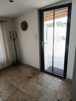 A room with a tiled floor, a door with a metal grill, a wall-mounted light switch, and a potted plant. - Quiet country home (Pernes-les-Fontaines)