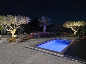 Une piscine à l’eau d’un bleu cristallin, entourée de parterres aménagés et d’arbres illuminés.