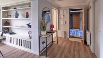 A modern hallway with a white console table, shelves with decorative items, a red lamp, and a door leading to another room.