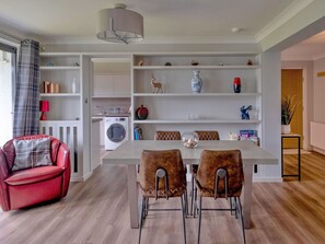 Een moderne keuken met witte kasten, een eettafel met twee stoelen, een rode bank en een wasruimte met een wasmachine.