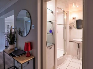Een moderne badkamer met een glazen douchecabine, een ronde spiegel en een klein wastafeltje.