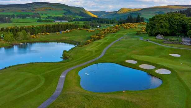 Ein Golfplatz mit Teich, einem Weg und Blick auf die umliegenden Hügel.
