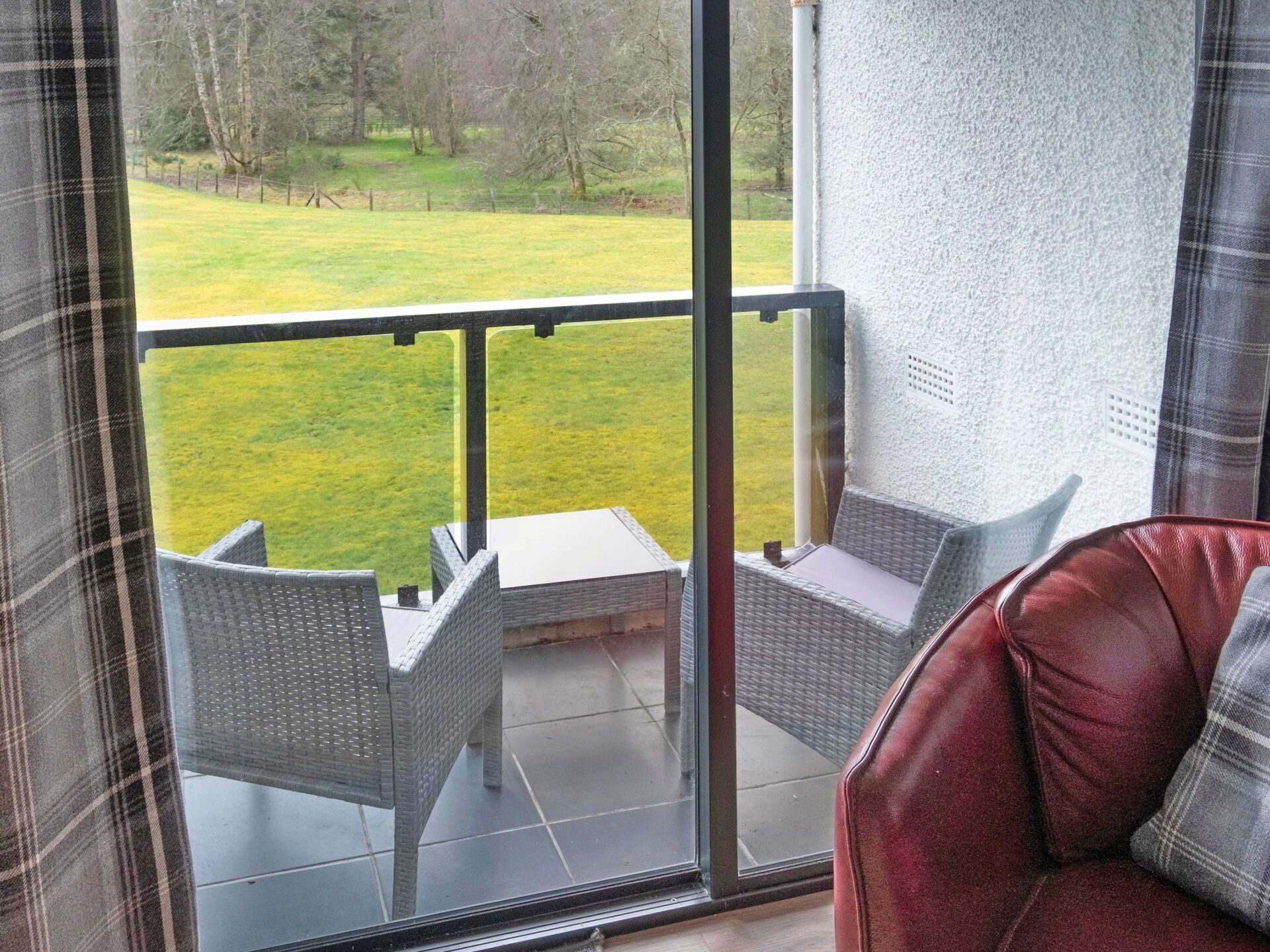 A balcony with wicker furniture and a view of a grassy area.