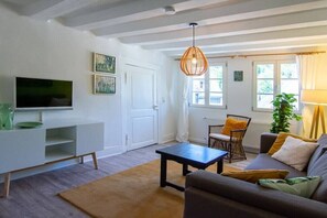 Ein Wohnzimmer mit einer Couch, einem Couchtisch, einem Fernseher, einem Korbstuhl und einem Fenster mit Vorhängen.