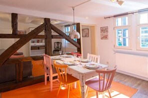 Ein Essbereich mit einem Tisch für vier Personen, Holzbalken darüber und einem Fenster mit Jalousien.
