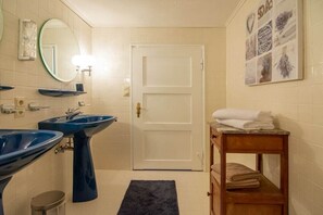 Ein Badezimmer mit zwei Waschbecken, einem Spiegel, einer Tür und einem Handtuchhalter.