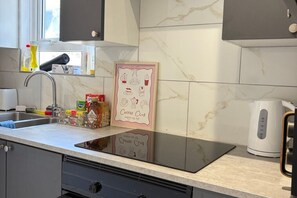 Une cuisine avec un dosseret en marbre, une œuvre d’art sur le thème du café, une bouilloire et divers ustensiles de cuisine disposés sur le plan de travail.