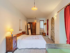 Ein Schlafzimmer mit einem Bett, Nachttischlampen, einer Holzkommode, einem Spiegel und einer Tür zu einem anderen Raum.