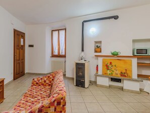 Ein Wohnzimmer mit einer Couch, einem Heizkörper, einem Heizgerät, einem Wandventilator, einem Fenster mit Vorhängen, einer Tür und einem Regal mit Teekanne und Mikrowelle.