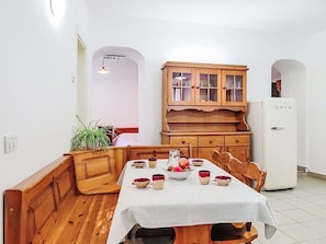 A dining area with a wooden table set for four, a cabinet with glass doors, and a white refrigerator. - Beautiful apartment for 2 guests (Porlezza)