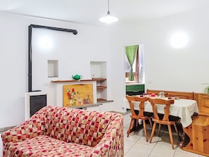 A living room with a sofa, a dining table with chairs, a green teapot on a shelf, and a window with curtains. - Cosy apartment for 2 guests (Porlezza)
