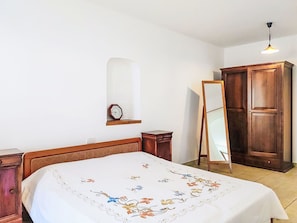 A bedroom with a bed, a wooden wardrobe, a mirror, and a wall clock. - Cosy apartment for 2 guests (Porlezza)