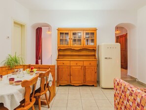 Cocina compacta con armarios de madera, una mesa de comedor con sillas, un refrigerador y un pequeño rincón de descanso.