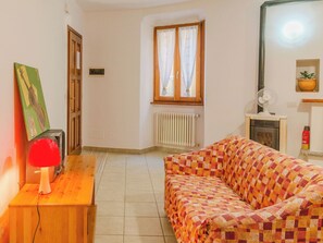 Ein Zimmer mit einer karierten Couch, einem Holztisch mit einer roten Lampe, einem Heizkörper, einem Fenster mit Vorhängen, einer Tür und einem Wandventilator.