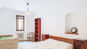 A bedroom with a bed, a wooden chair, a bookshelf, a radiator, a window, and a clock on the wall. - Lovely apartment for 2 people (Porlezza)
