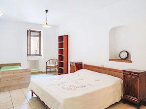 A bedroom with a bed, a wooden chair, a bookshelf, a radiator, a window, and a clock on the wall. - Beautiful apartment for 2 guests (Porlezza)