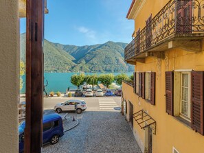 Ein Gebäude mit einem Balkon, der auf eine Straße mit geparkten Autos und eine Aussicht auf einen See und Berge blickt.