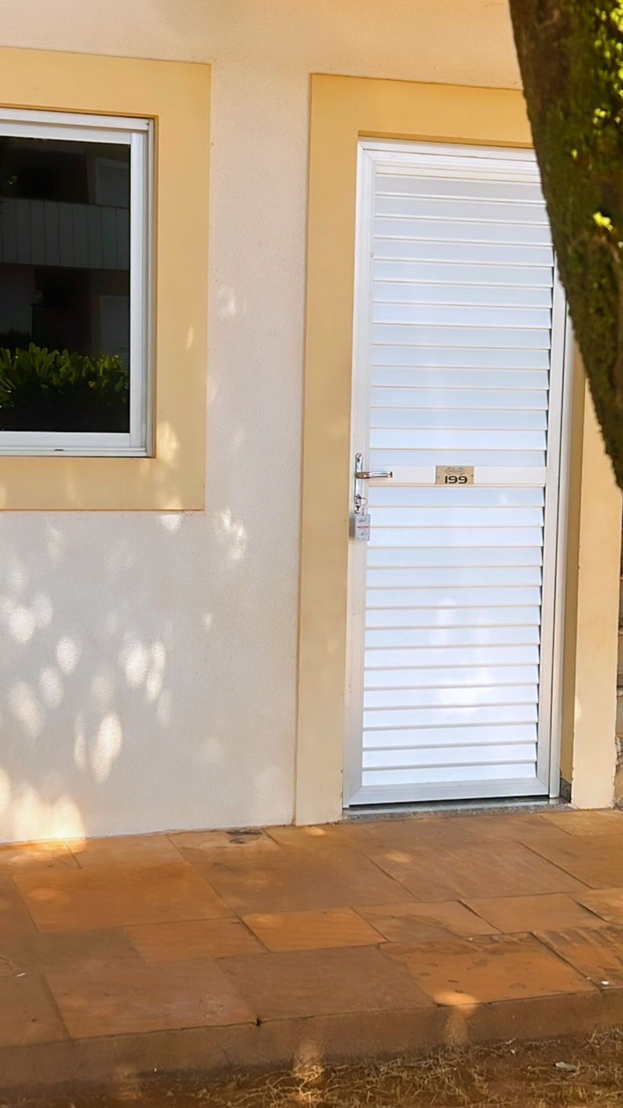 A closed white door with a number plate, a window with blinds, and a paved entrance.