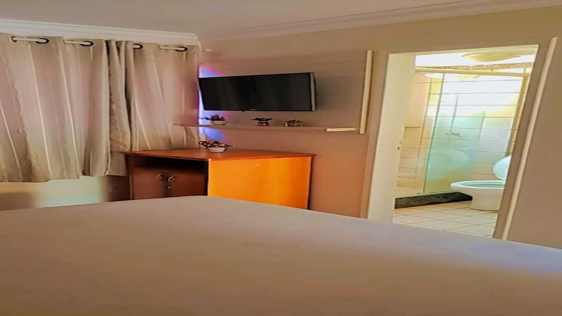 Una habitación de hotel con una cama, un televisor montado en la pared, un escritorio de madera y un baño visible a través de una puerta abierta.