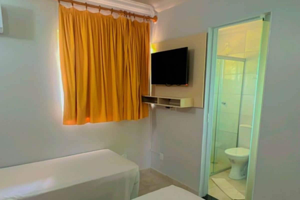 Ein Hotelzimmer mit zwei Betten, einem Fernseher und einem Badezimmer mit Glastür.