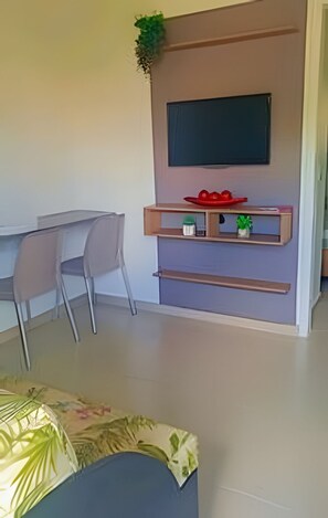 Uma sala de estar moderna com televisão de tela plana na parede, uma mesa de jantar com cadeiras e um pequeno aparador com objetos decorativos.