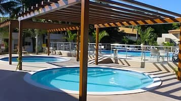 Área de piscina com duas piscinas circulares, um pergolado e espreguiçadeiras.