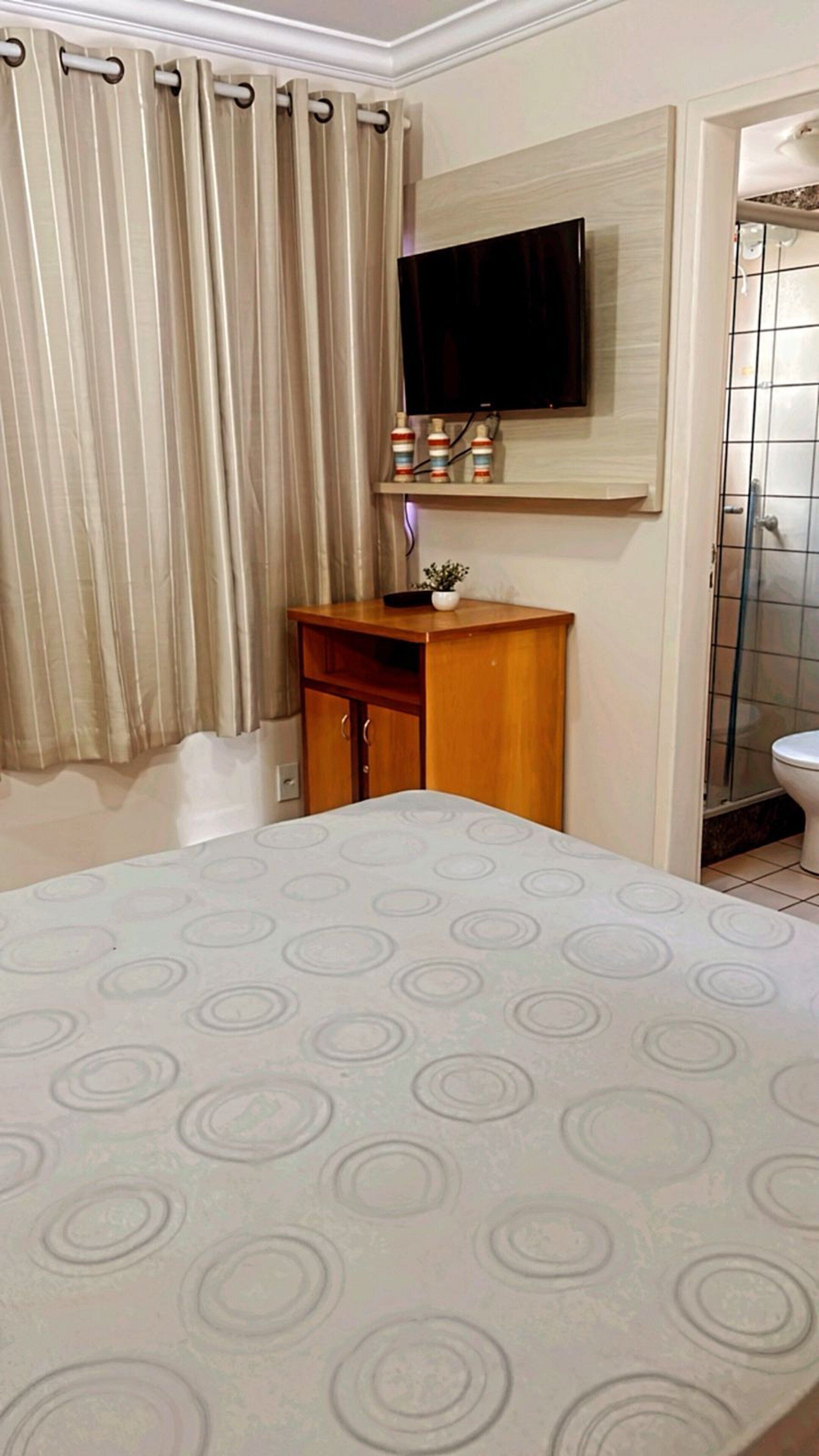 A hotel room with a bed, a wooden cabinet, a television mounted on the wall, and a shower area.