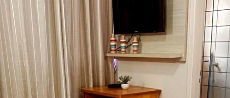A hotel room with a bed, a wooden cabinet, a television mounted on the wall, and a shower area.